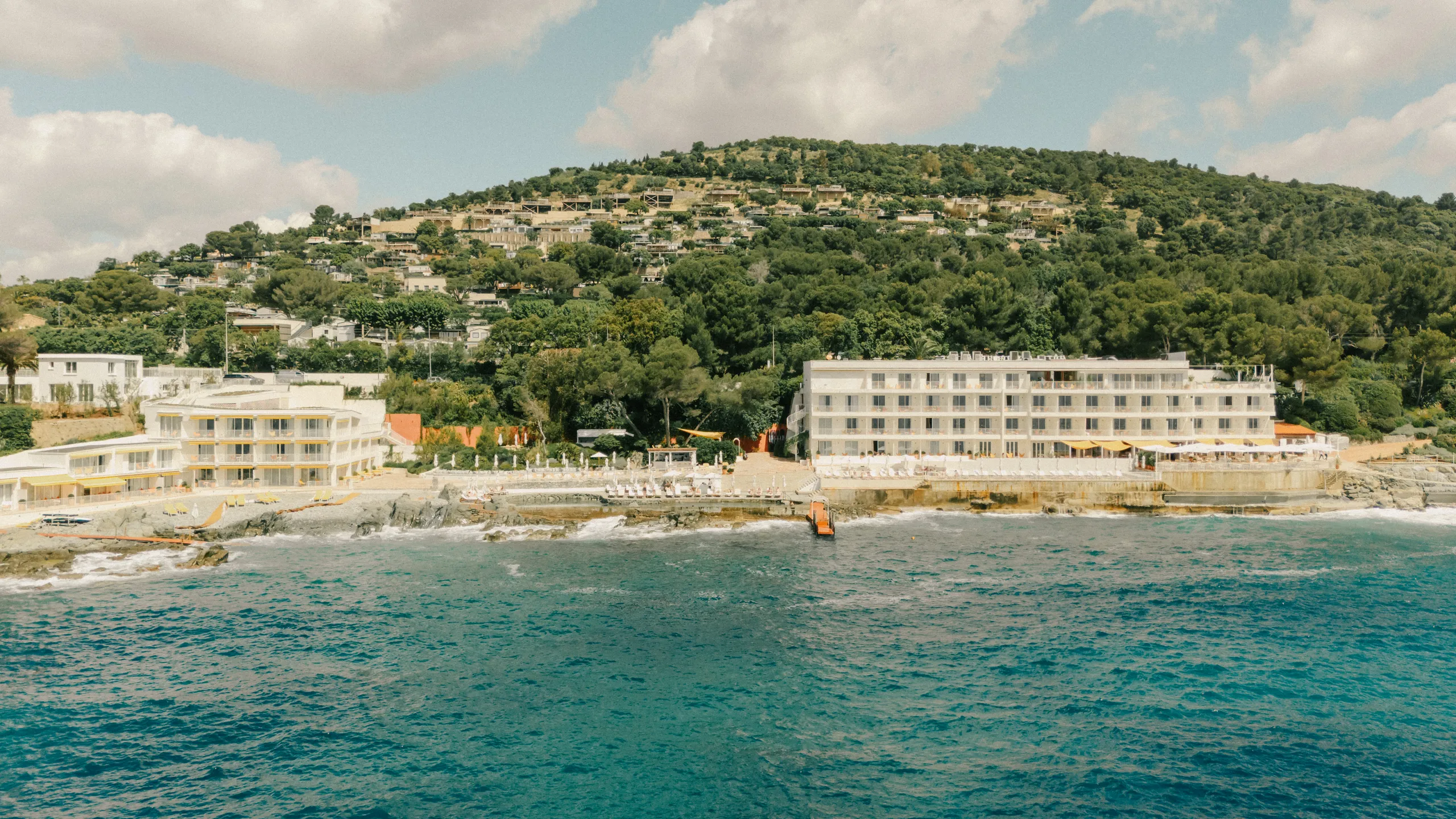 Low mid-century hotel above red coastal rocks and the sea